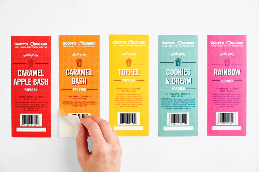 Five custom product labels printed in red, orange, yellow, blue and pink with a hand peeling the orange one.