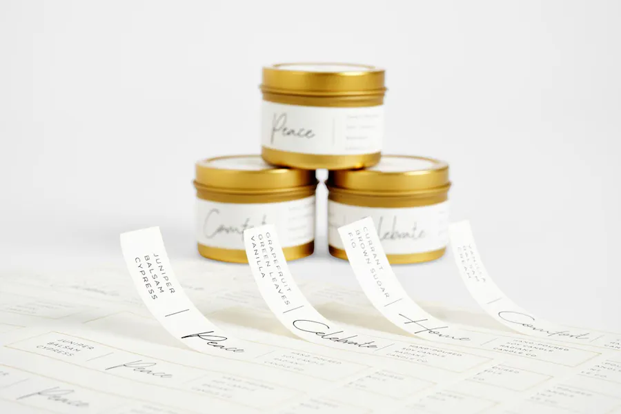 Custom product labels peeling off a backing sheet with a stack of three candles behind them.