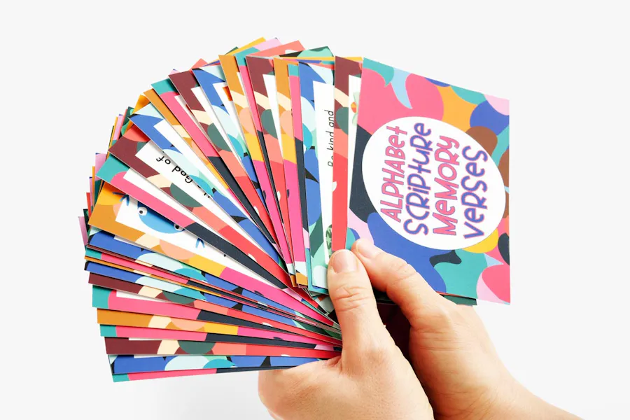 Two hands holding fanned-out scripture flashcards with a design in full color.