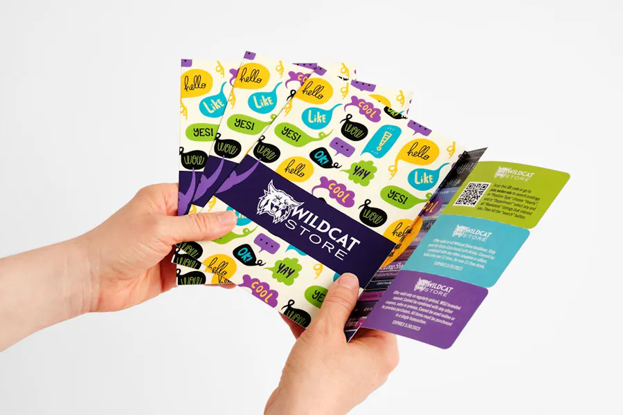 Two hands holding multiple mailers with perforated direct mail coupons in green, blue and purple.