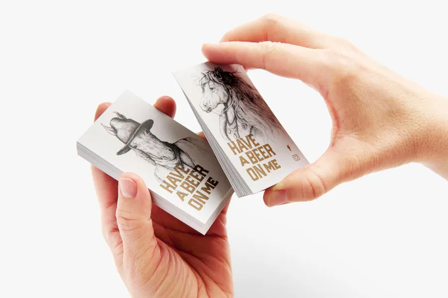 Two hands holding custom business cards printed with "Have a Beer On Me" and a horse design.
