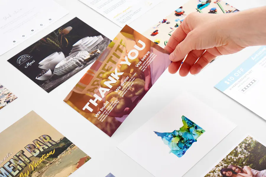 A hand laying down a custom postcard among various other printed postcards.