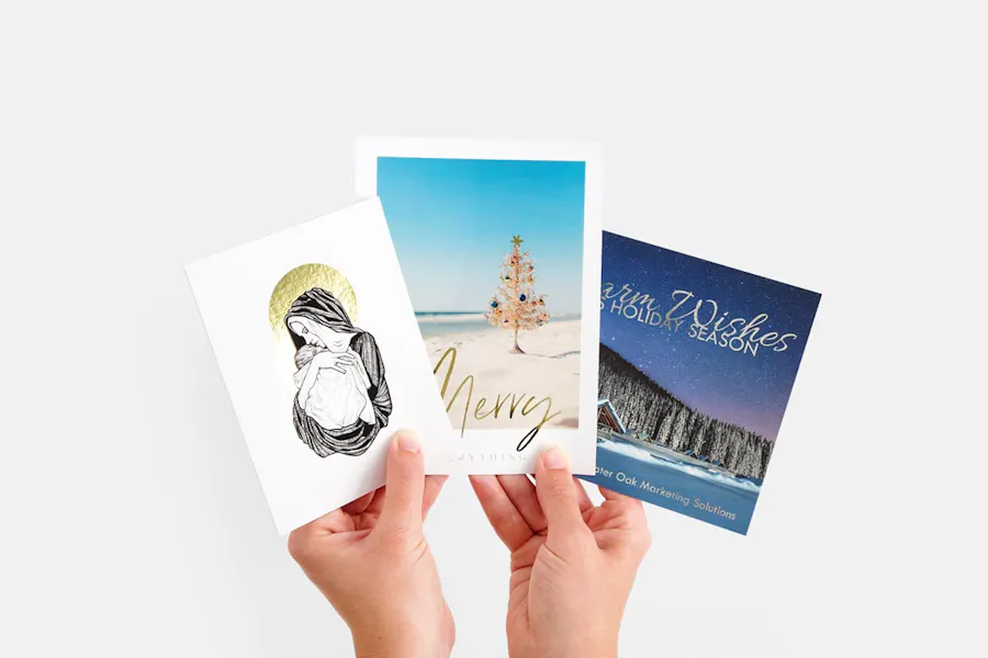 Two hands holding three fanned-out custom cards with holiday greetings and designs.