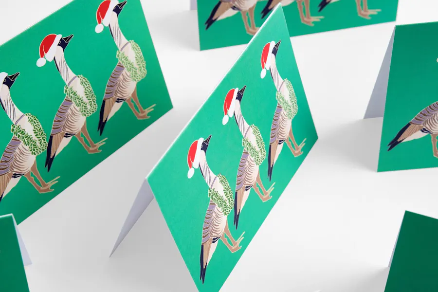 Six holiday greeting cards standing open with a green background and three festive geese on the front.