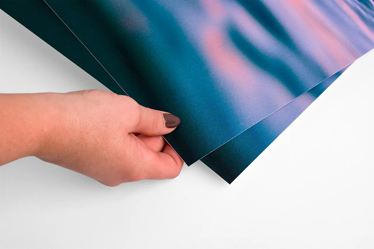 A hands holding the corner of post-consumer waste cardstock printed with a dark water scene.