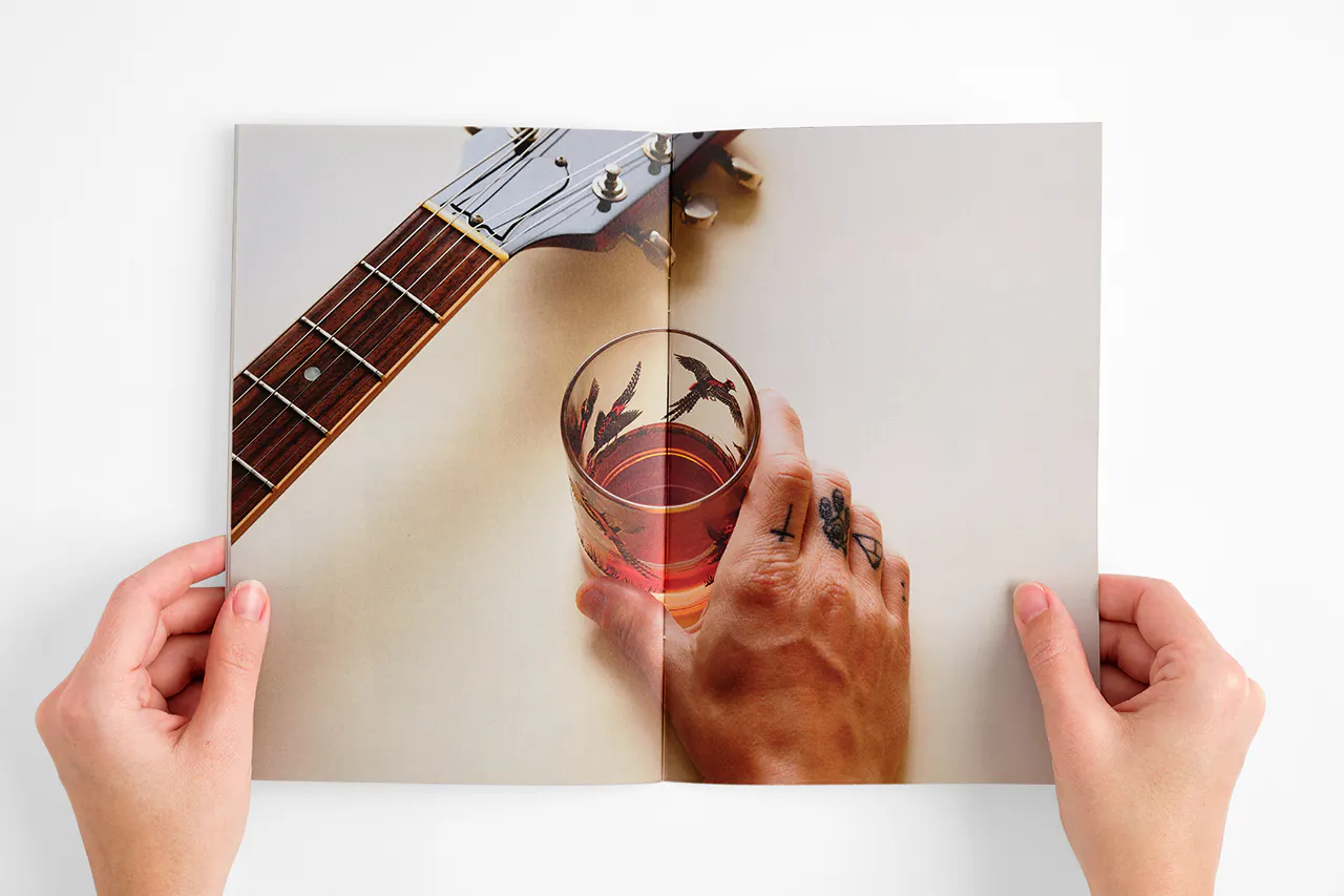 Two hands holding open an Oak & Eden marketing booklet to images of a glass of whiskey and a guitar.