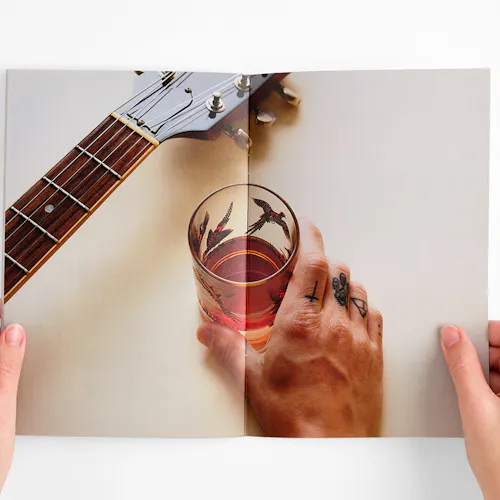 Two hands holding open an Oak & Eden marketing booklet to images of a glass of whiskey and a guitar.