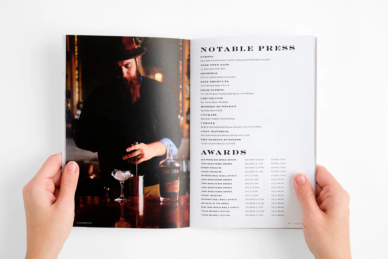Two hands holding open a brand book to an image of a bartender and press and awards for Oak & Eden whiskey.