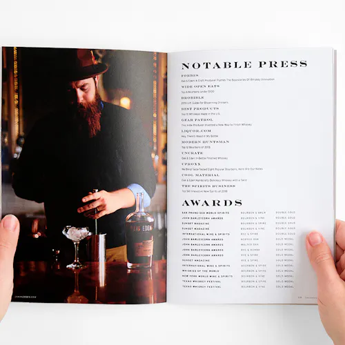 Two hands holding open a brand book to an image of a bartender and press and awards for Oak & Eden whiskey.