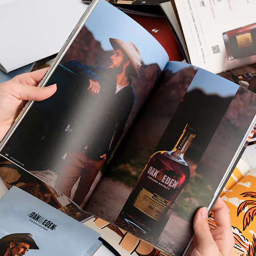 Two hands flipping through an Oak & Eden brand book with images of a man wearing a cowboy hat and a whiskey bottle.