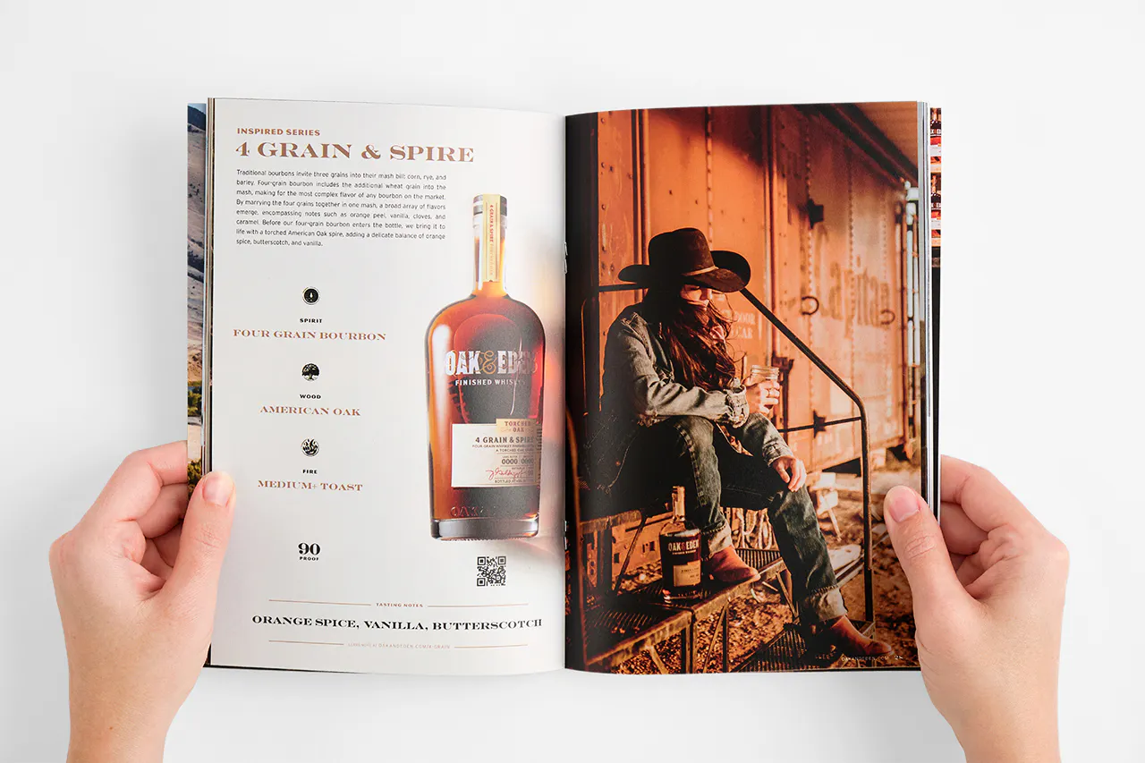 Two hands holding open an Oak & Eden booklet to an image of a woman sitting by a train car and details about whiskey.