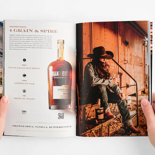 Two hands holding open an Oak & Eden booklet to an image of a woman sitting by a train car and details about whiskey.