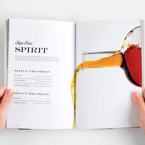 Two hands holding a marketing booklet open with an image of a bottle pouring whiskey and loyalty program details.
