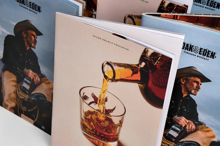 A group of custom booklets standing open with a cowboy and whiskey being poured into a glass on the covers.