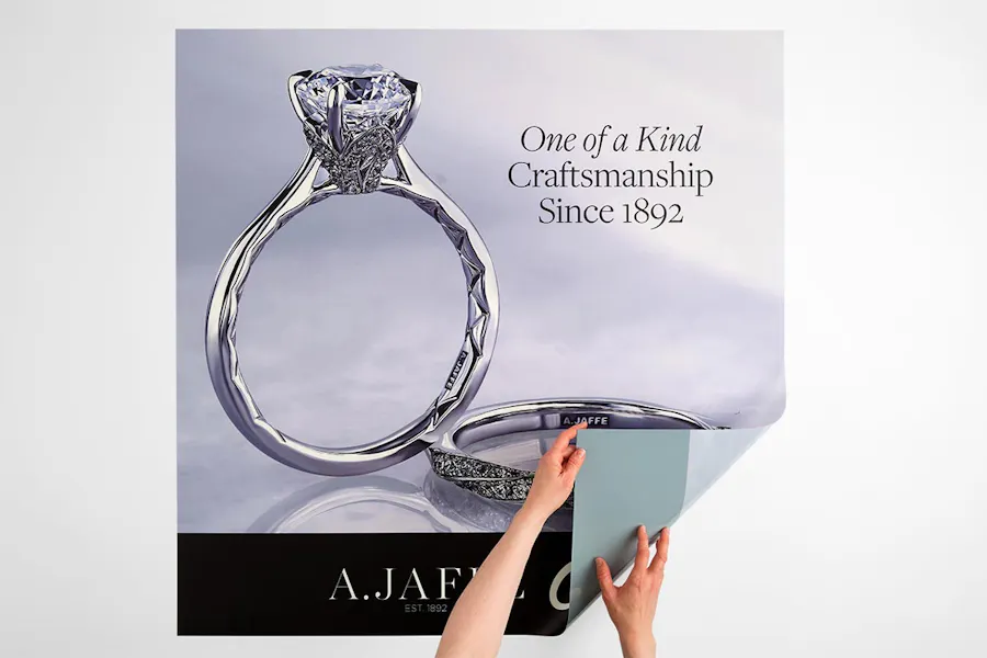 Two hands folding over the corner of a custom backlit sign printed with two silver rings for a jewelry store.