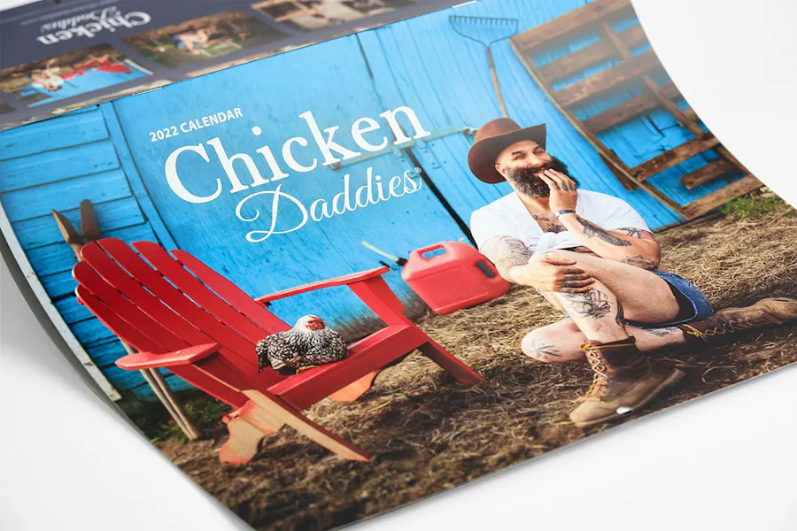 A saddle stitch calendar printed with Chicken Daddies and a man in shorts with a chicken on the cover.