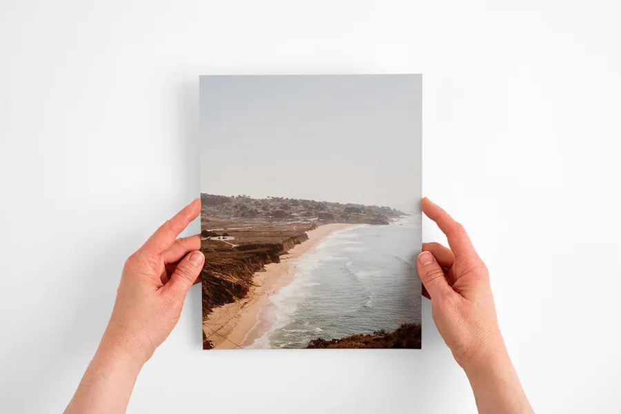 Two hands holding a custom card printed with a muted design of the ocean and a beach coastline.
