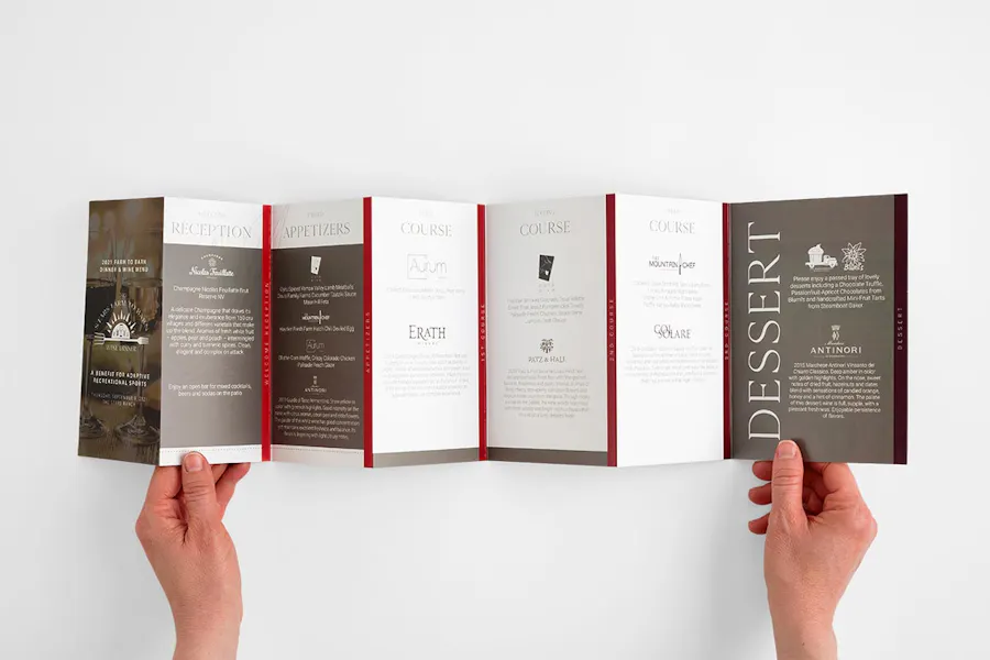 Two hands holding an unfolded stepped accordion brochure printed as a food and drink menu.