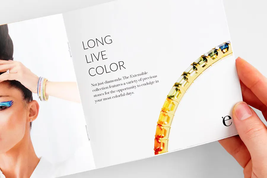A hand holding open a jewelry catalog with a saddle stitch binding with Long Live Color on the right page.