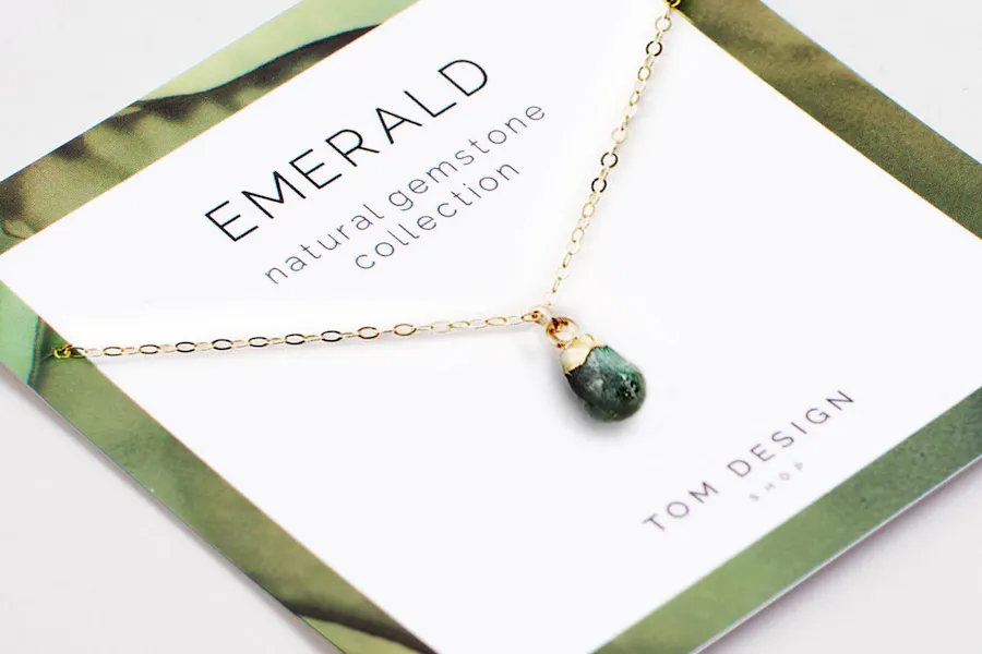 A custom jewelry backer with a green design, Emerald at the top and a necklace looped around it.