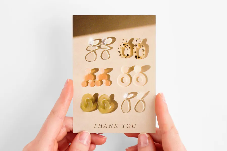 Two hands holding a product insert printed with six pairs of earrings and Thank You at the bottom.