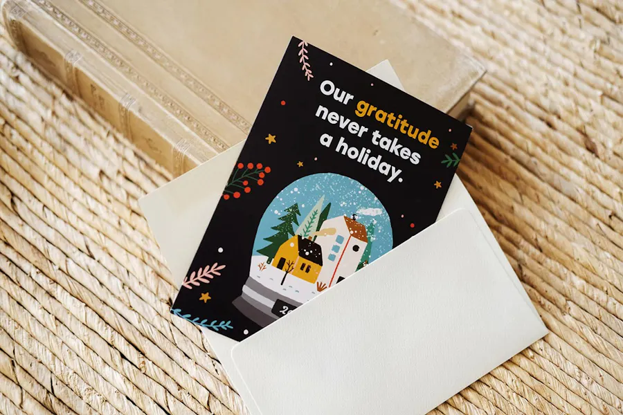 A custom thank you card with one corner in a white envelope and Our gratitude never takes a holiday. on the front.