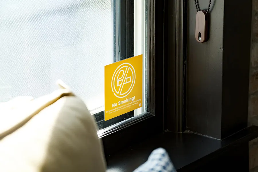 A yellow decal in the corner of a window with No Smoking! in white letters.