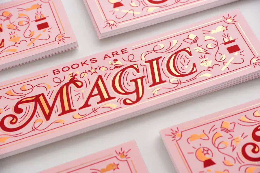 Stacks of custom printed foil bookmarks with a pink, red and gold design and Books Are Magic.