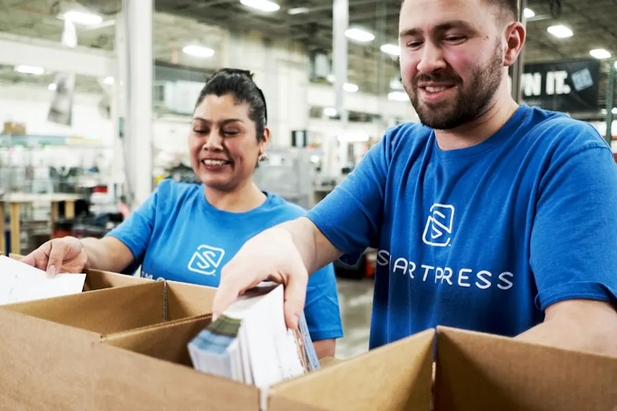 Two Smartpress employees in blue shirts putting custom print projects in packages boxes.