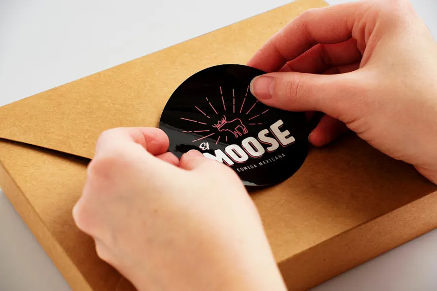 Two hands placing a label with Moose in white text on a takeout box.