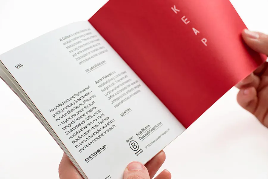 Two hands holding a marketing booklet printed with KEAP and a red background on the right and brand info on the left.