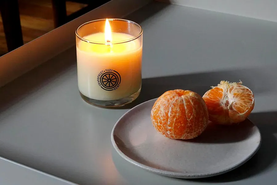 The Grapefruit+Yuzu candle from Keap next to a gray plate with two peeled clementines.