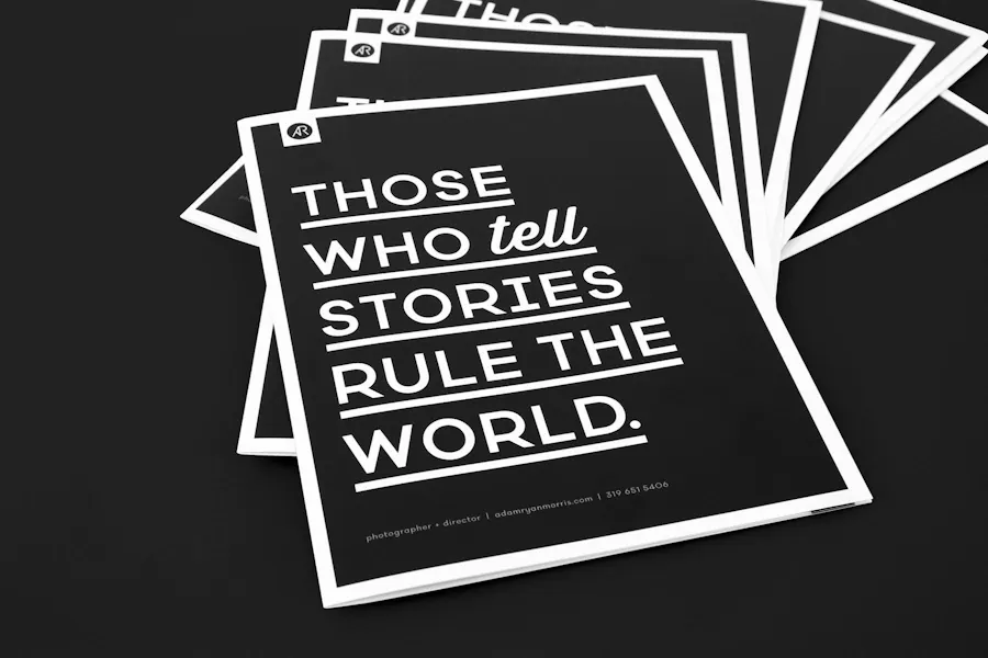 Custom saddle stitch booklets fanned out with a black and white design and Those Who Tell Stories Rule The World.
