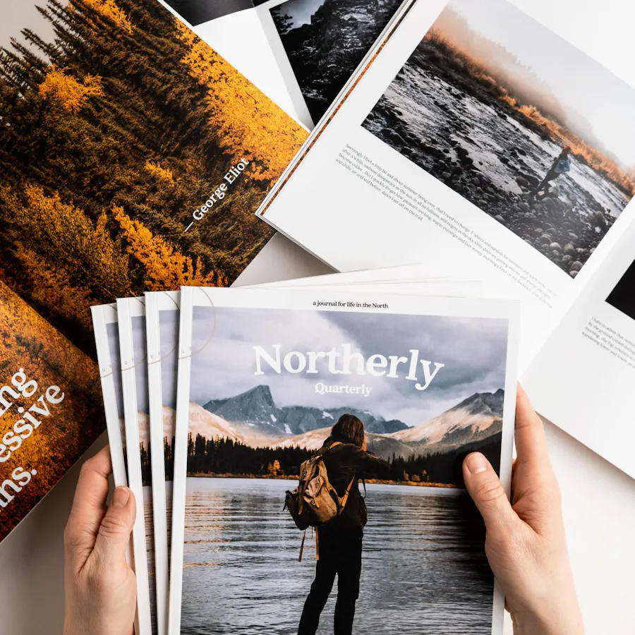 Two hands holding a stack of Northerly magazines above more custom magazines laying open.