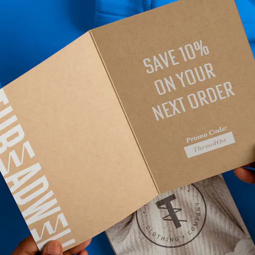 Two hands holding open a card printed on Kraft paper and with Save 10% On Your Next Order in white.