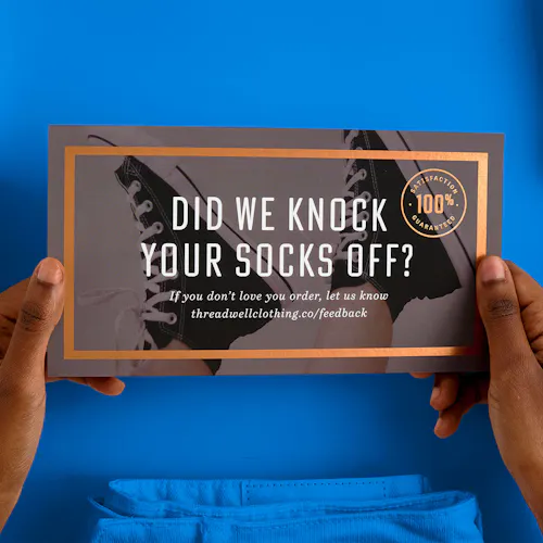 Two hands holding a custom package insert printed with Did We Knock Your Socks Off? in white.