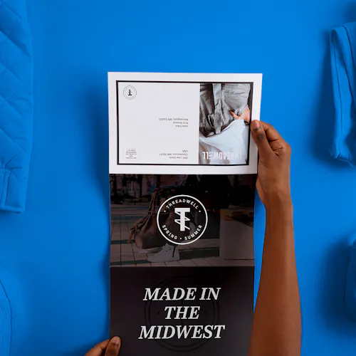 Two hands holding an unfolded direct mail brochure printed with Made in the Midwest and Threadwell Clothing Company.