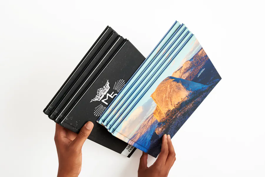 Two hands holding hardcover books with a vertical orientation and a horizontal orientation.