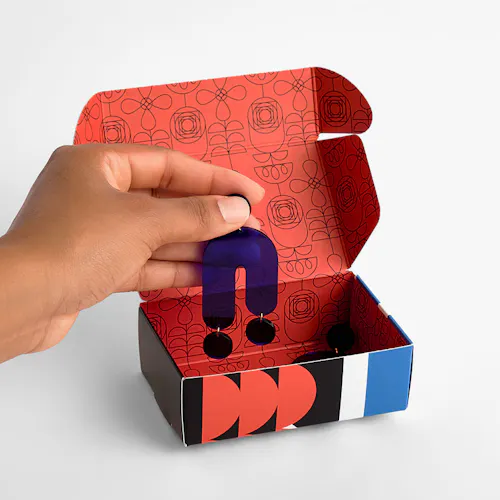 A hand holding a black dangling earring above a custom printed box with the lid open.