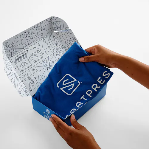 Two hands holding a folded Smartpress T-shirt above a custom printed tuck box with a blue and white design.