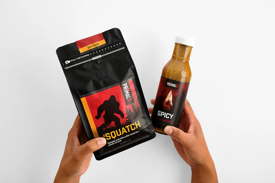 Two hands holding a bottle of hot sauce and a bag of coffee with custom labels printed with a red and black design.