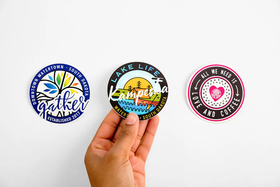 Three round stickers in a row with creative print designs and a hand holding the middle sticker.