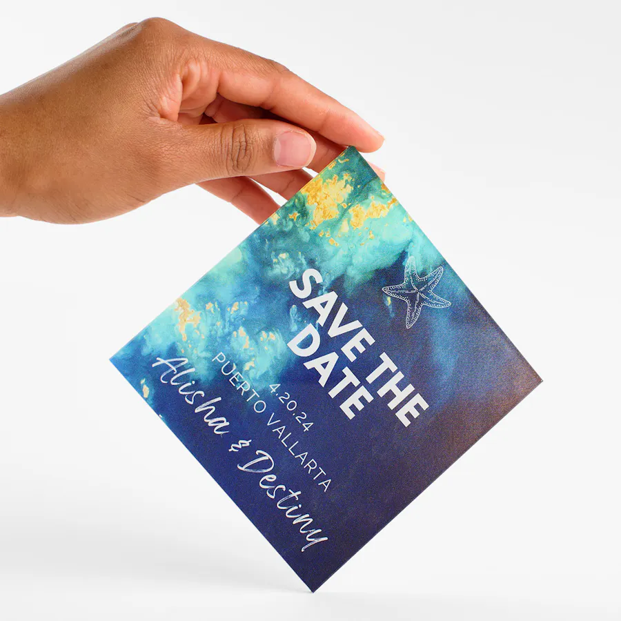 A hand balancing a custom clear sign on its corner and printed with Save the Date and a blue ocean design.