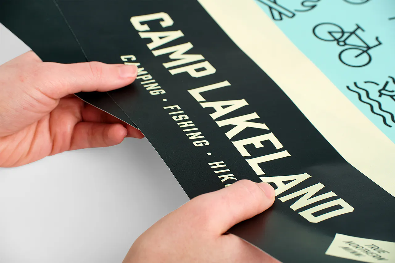 Two hands holding a smooth wall decal printed with Camp Lakeland.