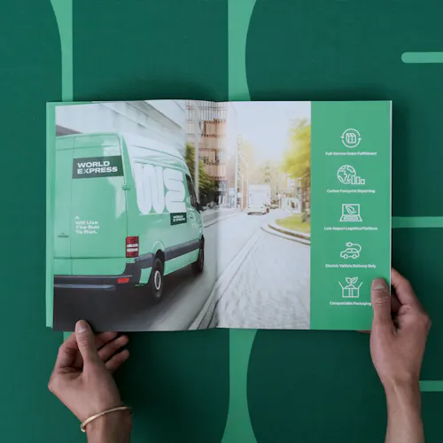 Two hands holding open a product catalog for a trade show with an image of a green van on the inside.