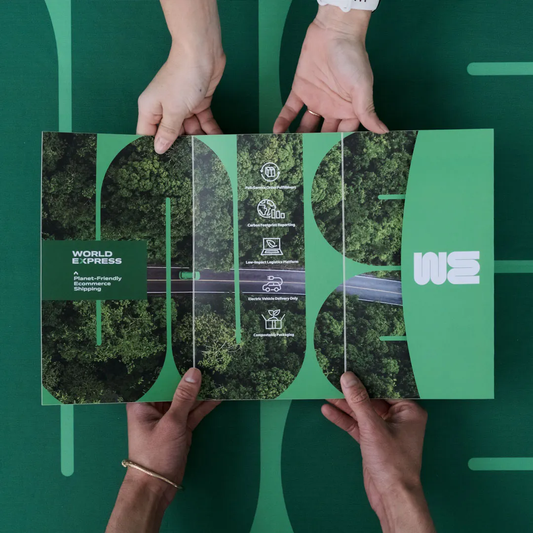 Four hands holding open a tri-fold pocket mailer with a green design and tree imagery.