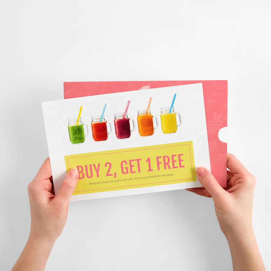 Two hands holding a white insert card with "Buy 1, Get 1 Free" in pink on top of a pink mailer envelope.