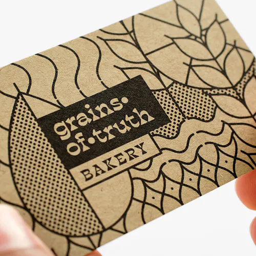 Two hands holding a business card printed on Kraft paper with Grains of Truth Bakery on the front.