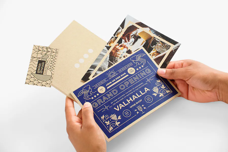 Two hands holding custom invites, a booklet and business card printed on Kraft paper.