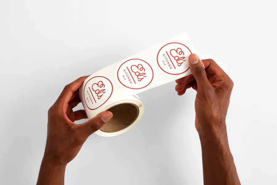 Two hands holding a roll of custom labels with a round design and Ed's Kitchen in red.